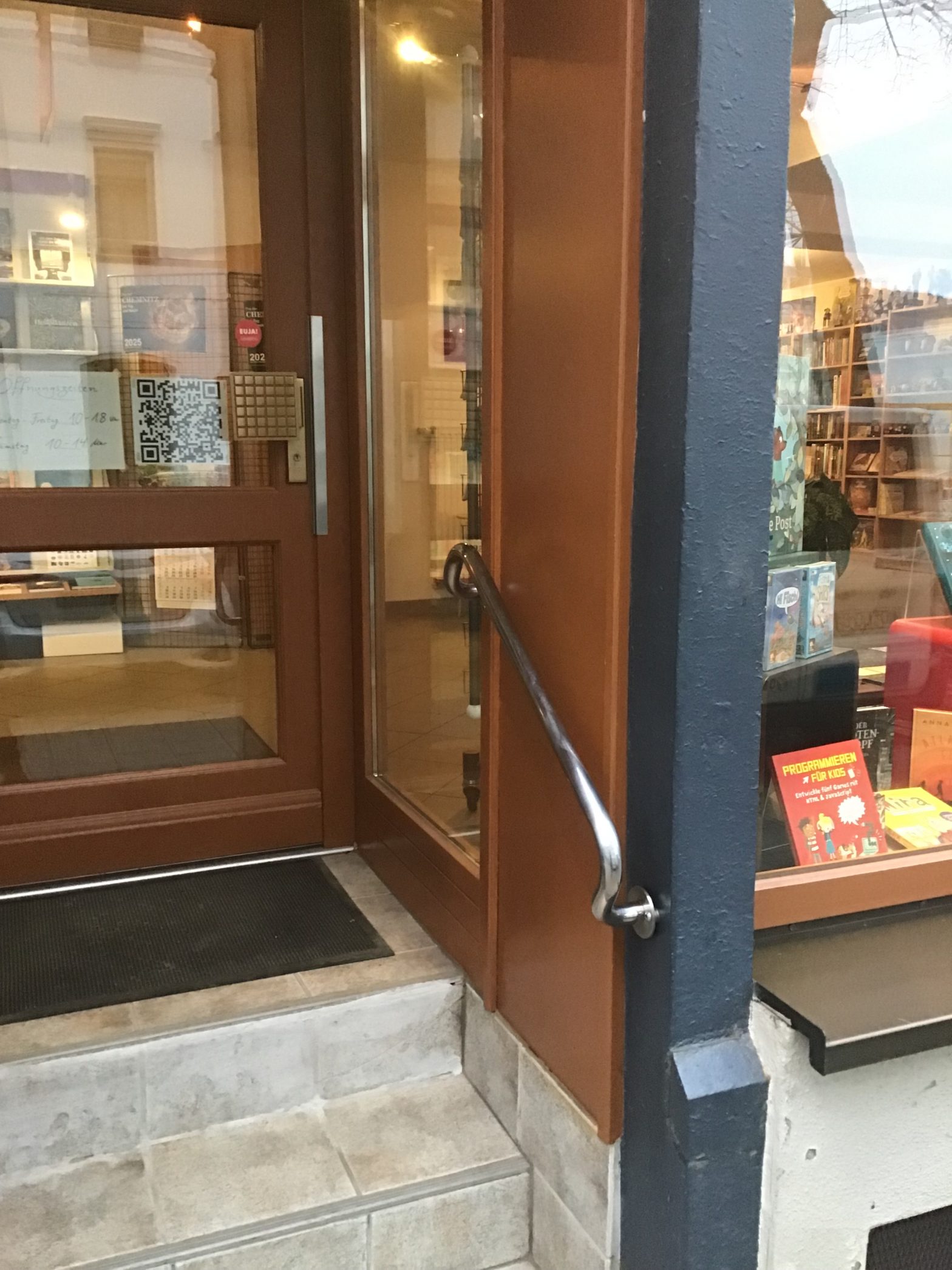 Eine Foto vom Eingangsbereich der „Buchhandlung am Brühl“. Auf der rechten Seite sieht man ein metallfarbenes Geländer.