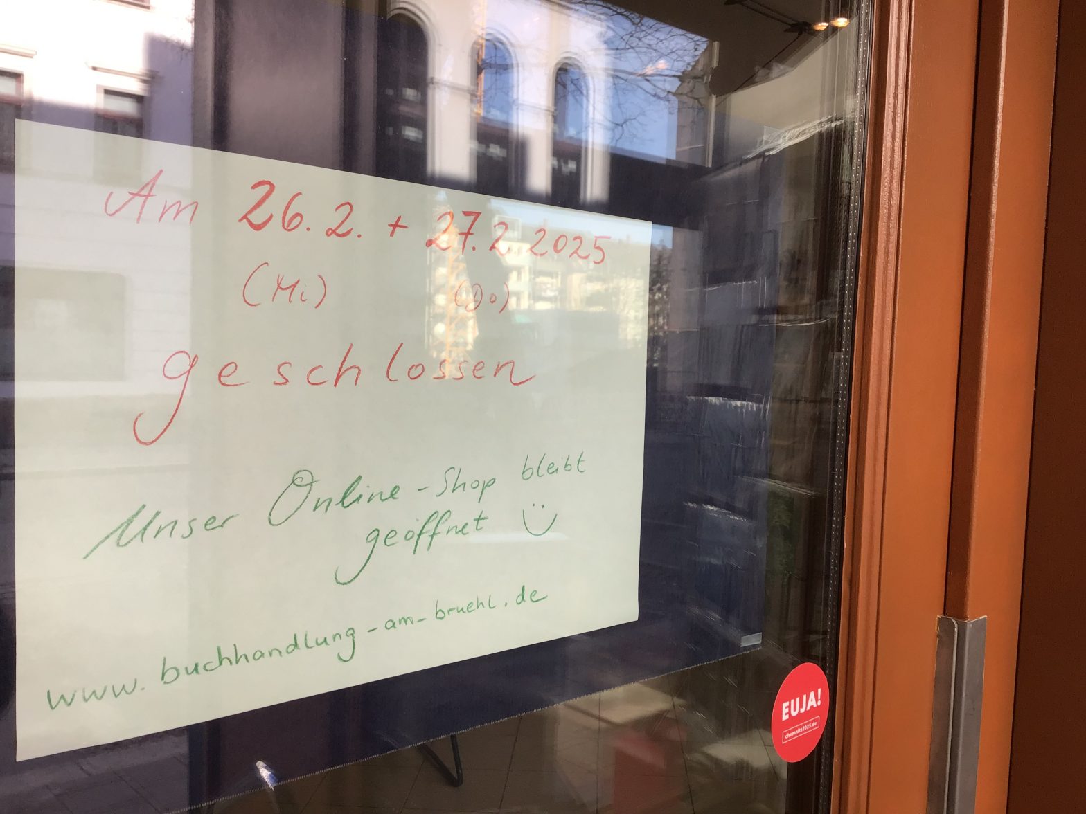 Ein Plakat von innen befestigt an der Eingangstür der Buchhandlung am Brühl. Auf dem Schild steht, dass die Buchhandlung am 27. und 26.2. geschlossen ist, der Onlineshop aber weiterhin geöffnet ist.