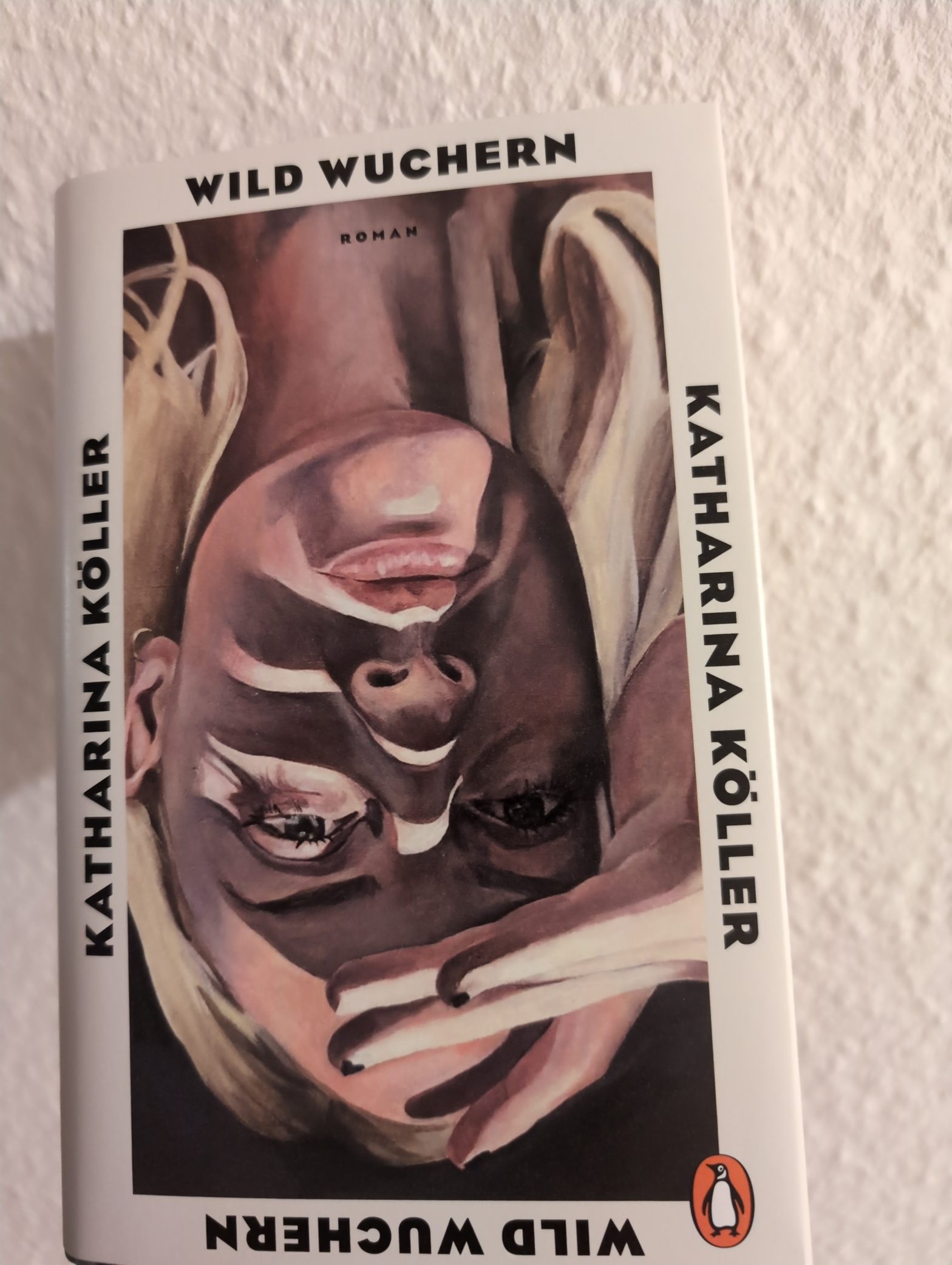 Das Cover von "Wild Wuchern" von Katharina Köller. Das Bild einer blonden Frau im Stil eines Ölgemäldes. Das Bild steht Kopf. Umrahmt ist das Bild von einem weißen Rand. Links und rechts steht der Name der Autorin in schwarzer Schrift. Oben und unten der Name des Titels, so dass man den Titel lesen kann, auch wenn das Buch auf dem Kopf steht.