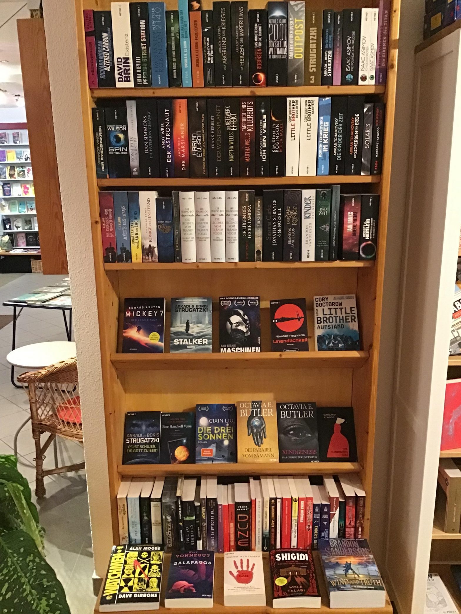 Ein Foto des Scifi- und Fantasyschranks in der Buchhandlung am Brühl in Chemnitz. In einem Holzschrank stehen viele Bücher. Auf den oberen drei Regalbretten sieht man nur die Buchrücken. Darunter sind zwei Displayreihen. Hier sieht man Bücher wie „The Handmaid‘s Tale“ von Margaret Atwood und „Die Parabel vom Sämann“ von Octavia Butler. Darunter kommt noch einmal eine Reihe mit Buchrücken. Darunter folgt noch eine Displayreihe mit Büchern wie Naomi Aldermans „Die Gabe“ und „The Wind and Truth“ von Brandon Sanderson.