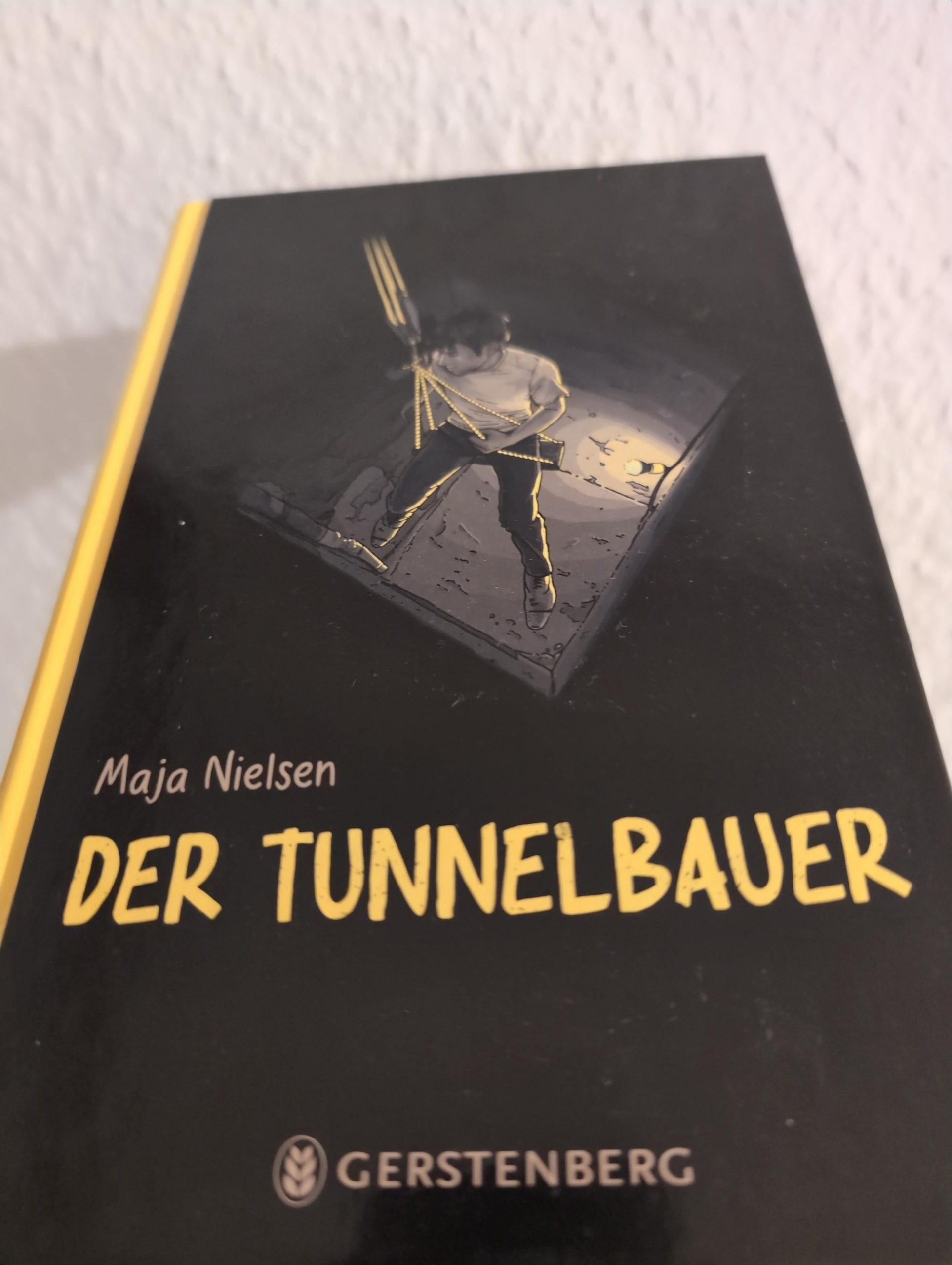 Das Buchcover von "Der Tunnelbauer". Man sieht einen jungen Mann, der sich in einen Schacht hinein abseilt.