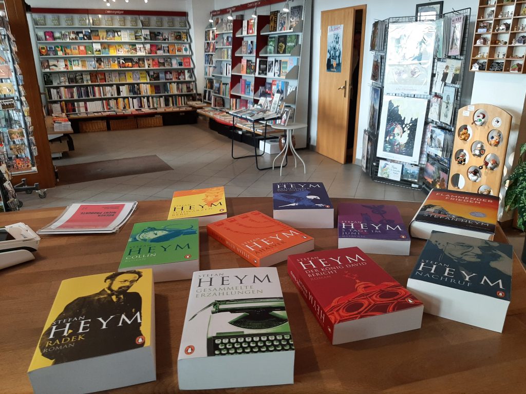 Zu sehen sind viele verschieden Bücher von Stefan Heym auf dem Tresen der Buchhandlung am Brühl. Im Hintergrund sieht man Teile des Ladens, u.a. die "Romandwand".
