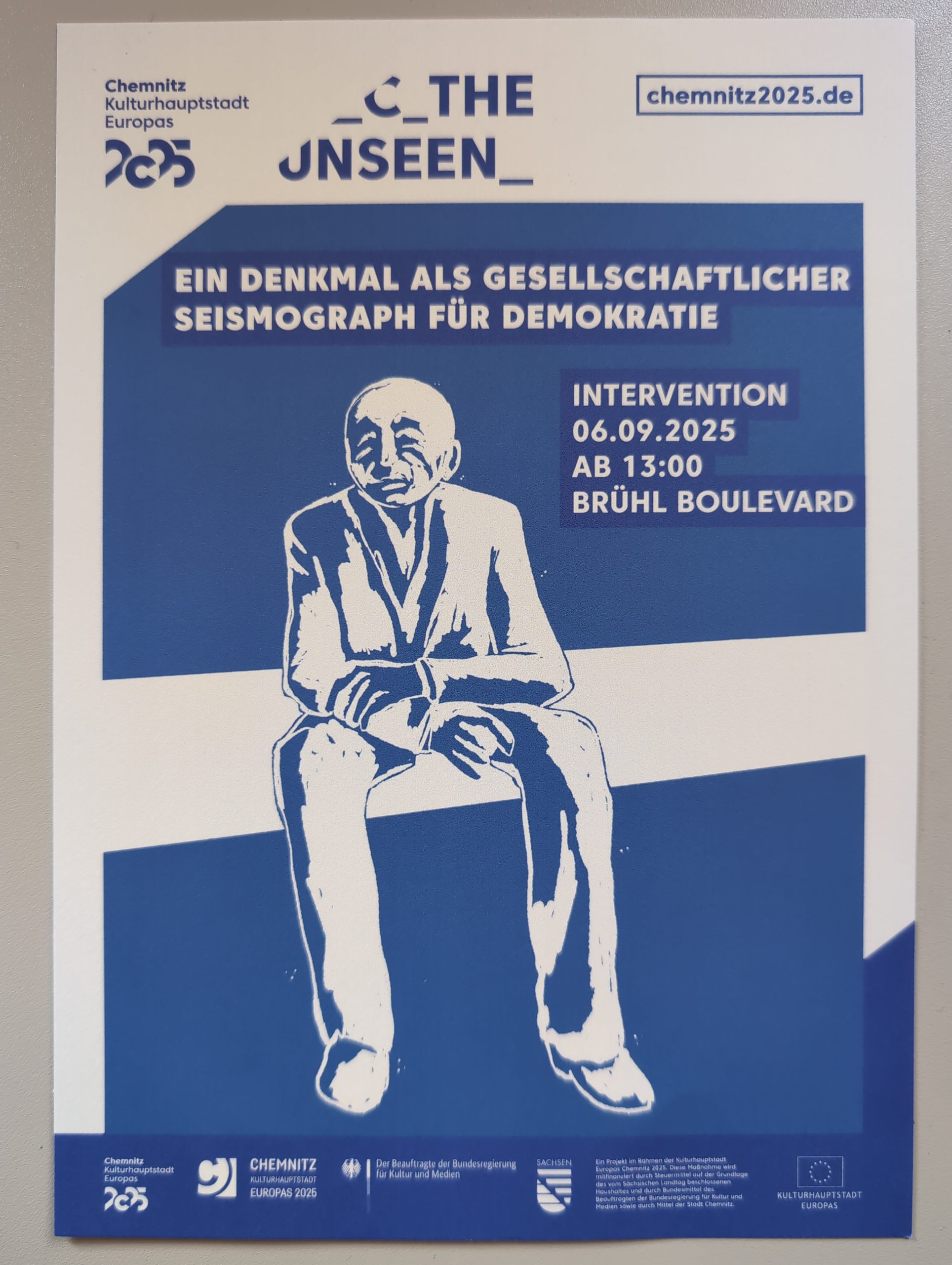 Der Flyer zu Ehren Justin Sanders. Der Flyer ist in blau und weiß gehalten. Zu sehen ist die Statue stilisiert als Druck.