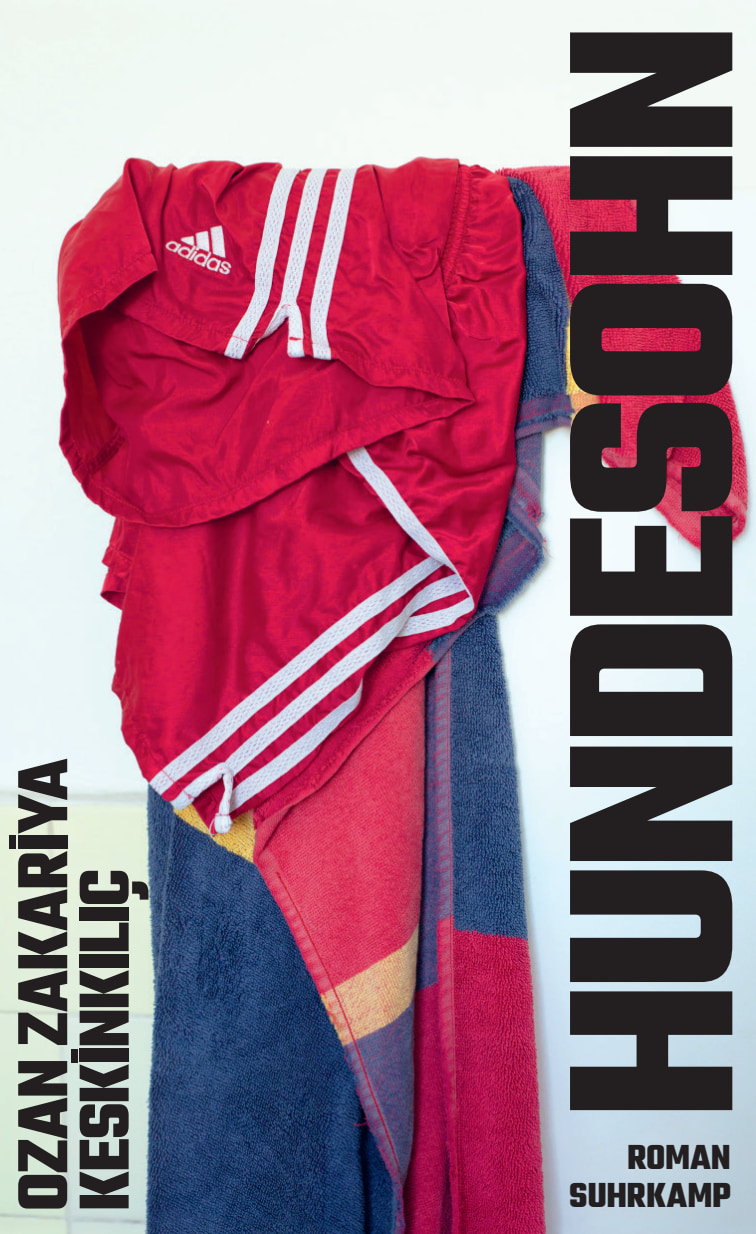 Zu sehen ist das Cover von "Hundesohn". Der Hintergund des Covers ist in weiß gehalten. In schwarzer Schrift steht der Namen des Autors (Ozan Zakariya Keskinkılıç) und der Titel des Buches sowie "Roman Suhrkamp" auf dem Cover. Die Schrift verläuft dabei von oben nach unten an den Rändern des Covers. Der Titel ist sehr groß gehalten. Zwischen der Schrift, in der Mitte des Covers, ist ein roter Jogginganzug aus Polyester zu sehen, der in ein Baumwollhandtuch übergeht, das an eine Nationalflagge erinnert, jedoch keinem Land eindeutig zuzuordnen ist.