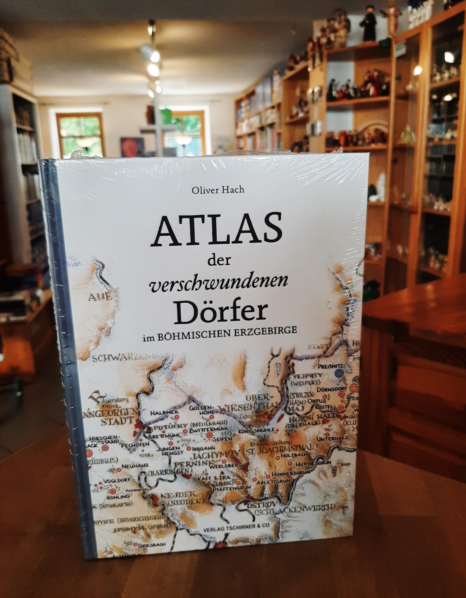 Auf dem Bild zu sehen ist der in dem Verlag Tschirner & Co erschienene "Atlas der verschwundenen Dörfer im böhmischen Erzgebirge". Im Hintergrund sieht man leicht verschwimmen die Regale der Buchhandlung am Brühl mit erzgebirgischem Kunsthandwerk.